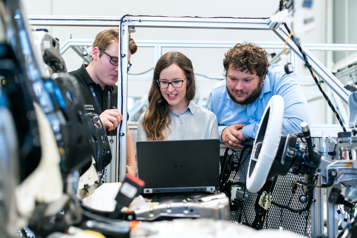 Three engineers reviewing a design together on a laptop beside a test rig